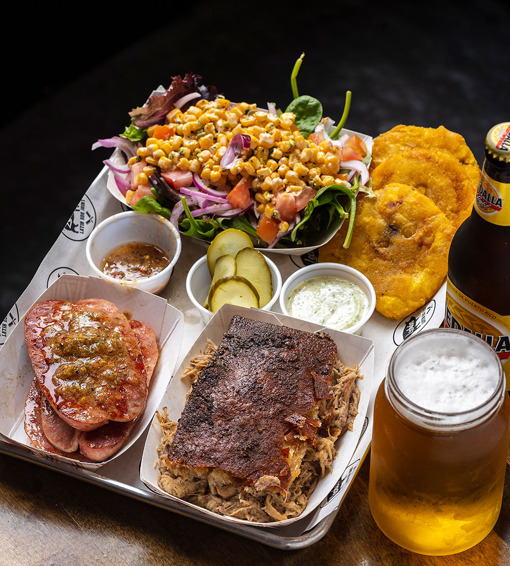 The signature Lechon served in classic Carolina meat-and-three style, with elote corn salad, argentinian sausages, tostones, and lots of condiments.